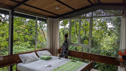 a woman standing in a room with a bed in front of windows at Sinharaja Kurulu Ella Eco Resort in Deniyaya