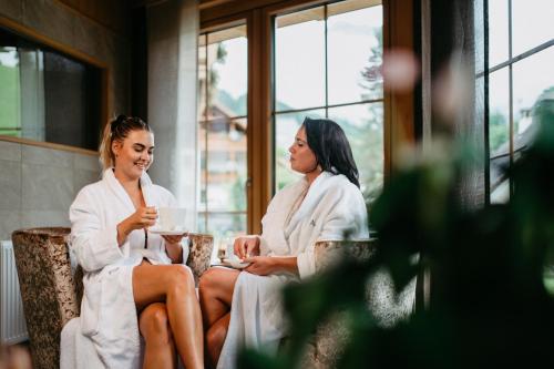 two women sitting in robes talking in a room at ALMHOF Alpin Apartments & Spa in Dienten am Hochkönig