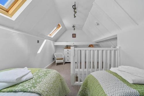 a white attic bedroom with two beds and a crib at The Stables Rectory Farm in Halstead