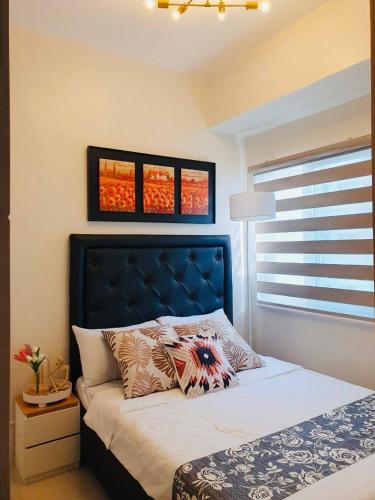 a bedroom with a bed with a blue headboard and windows at 1 Br CONDO Vine Residences Quezon City with POOL NETFLIX WIFI VIDEOKE BOARD GAMES in Manila