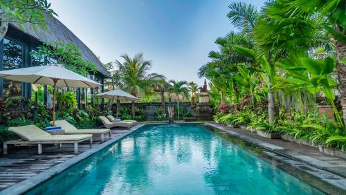 a pool with chairs and umbrellas next to a house at Gayatri Retreat Ubud in Ubud