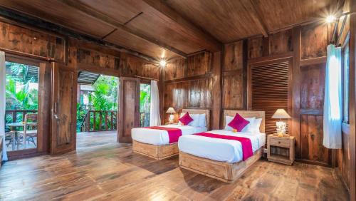 two beds in a room with wooden walls at Gayatri Retreat Ubud in Ubud