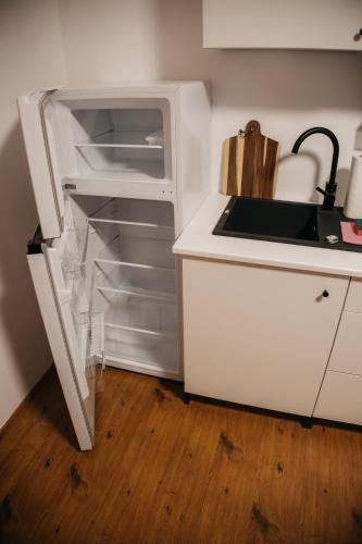 a white kitchen with a sink and an open refrigerator at Macao Apartmani in Vinkovci