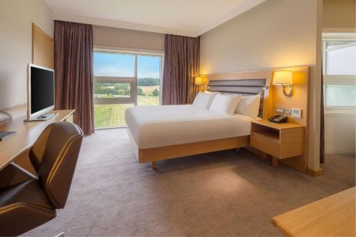 a hotel room with a bed and a desk and a television at Hilton at St George's Park in Burton upon Trent