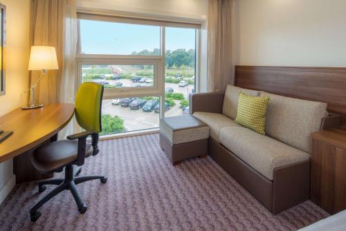 a hotel room with a couch and a desk and a window at Hilton at St George's Park in Burton upon Trent