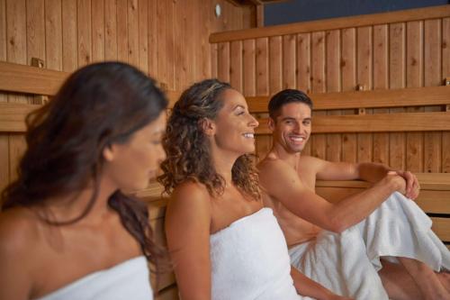 a man and two women sitting in a sauna at Hilton at St George's Park in Burton upon Trent
