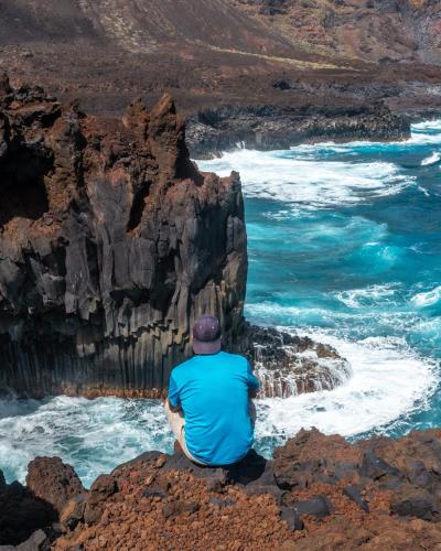 a man sitting on the rocks looking at the ocean at La Casita a 60 pasos del mar in Tamaduste