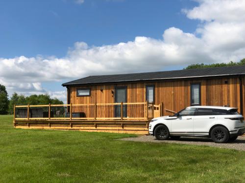 un coche blanco estacionado frente a una casa de madera en Shropshire Lodges - Romantic Luxury Hot Tub Breaks en Bridgnorth