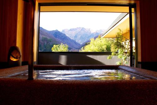 a bath tub with a window with a view of mountains at Super Hydrogen Rich Spa Yado Kanzan in Minakami