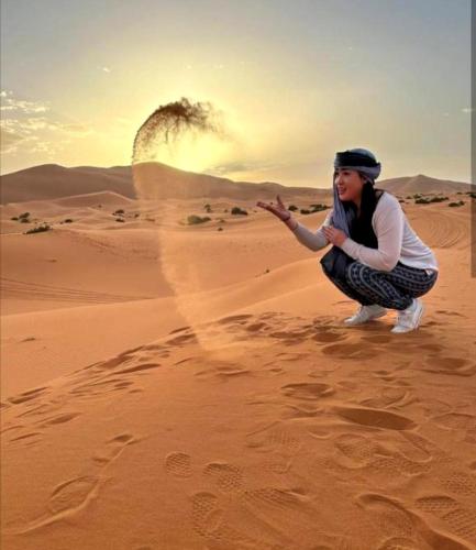 a woman is squatting in the desert at Enjoy Luxury Camp in Merzouga