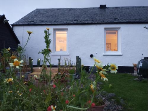 a white house with flowers in the yard at Snowberry Cottage in Borve