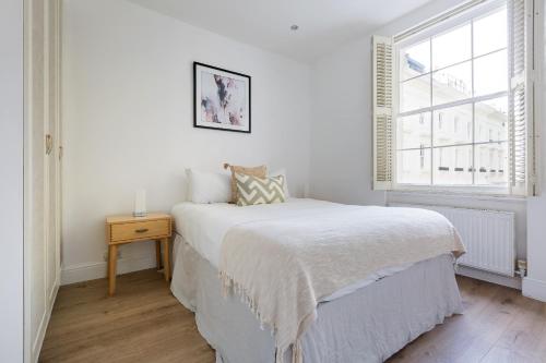 een witte slaapkamer met een bed en een raam bij Cozy and bright 1 bedroom apt in Knightsbridge in Londen