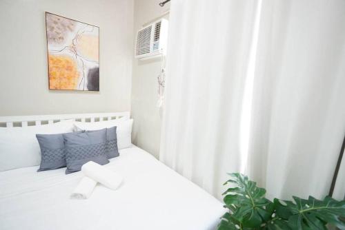um quarto branco com uma cama branca com almofadas azuis em Comfy Studio near Shaw MRT EDSA w/ Wi-Fi & Netflix em Manila