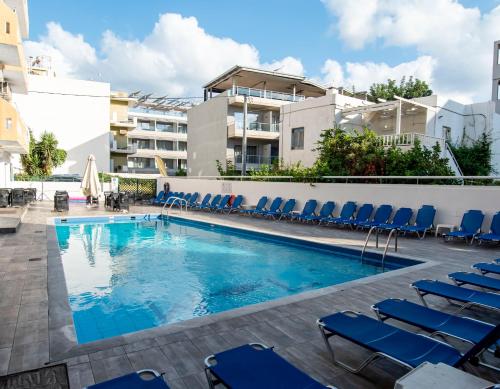 une piscine avec des chaises bleues et un bâtiment dans l'établissement Pela Maria Hotel, à Chersónissos