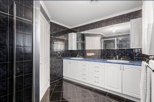 baño con 2 lavabos y paredes de azulejos negros en 5 bedroom home in a quiet area en Mill Park