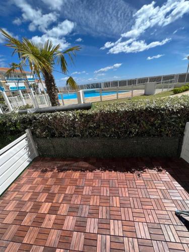 une terrasse en briques avec une clôture et un palmier dans l'établissement T3 front de mer avec piscine, à Frontignan