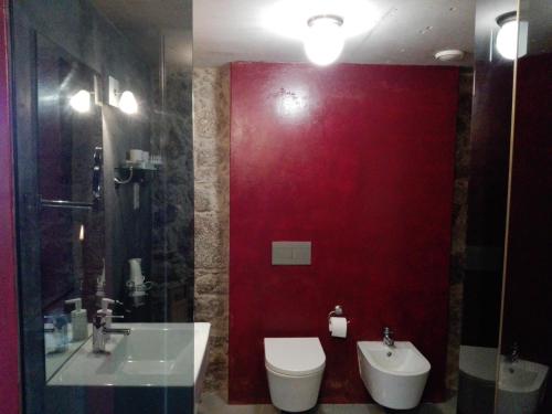 baño con pared roja, aseo y lavamanos en Casas da Quinta da Cancela en Balugães