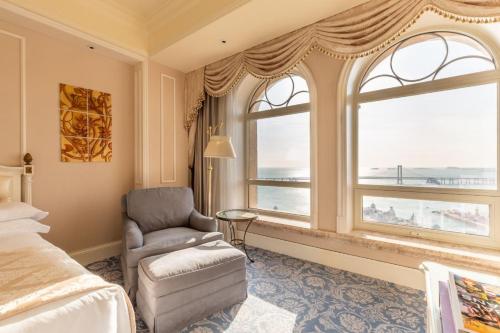 a bedroom with a bed and a chair and windows at The Castle Hotel, a Luxury Collection Hotel, Dalian in Dalian