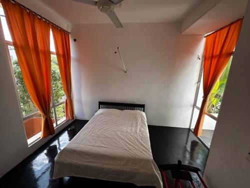 1 dormitorio con 1 cama y 2 ventanas con cortinas de color naranja en Mango Tree Villa, en Sri Jayewardenepura Kotte