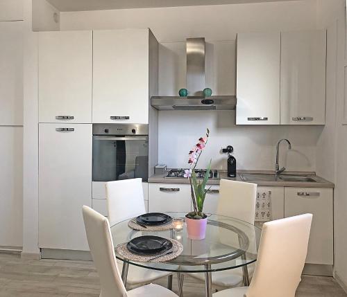 cocina con mesa de cristal y armarios blancos en FamilyBO Apartments Bologna Delight - front station, en Bolonia