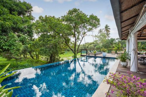 a swimming pool in front of a house with trees at Sol De Goa in Nerul
