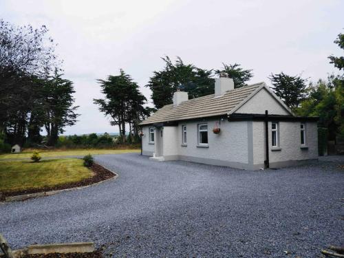 a small white house on a gravel driveway at Ballybur Cottage in Kilkenny