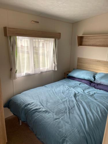 a bedroom with a blue bed and a window at Emeralds caravan lettings in Selsey
