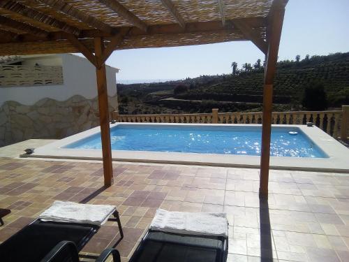 uma piscina com duas cadeiras debaixo de uma pérgula de madeira em Casa rural CAÑADA PAEZ em Vélez-Málaga