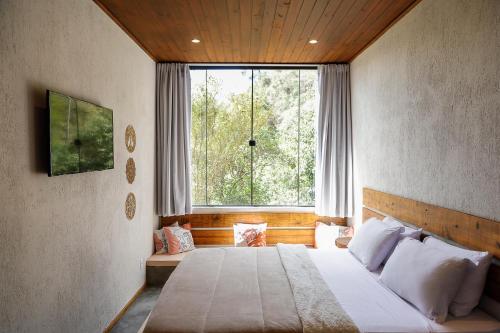 ein Schlafzimmer mit einem Bett und einem großen Fenster in der Unterkunft Vista do Vale lofts - Itaipava in Petrópolis