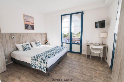 a hotel room with a bed and a desk and window at Hotel Mercedes in Hossegor