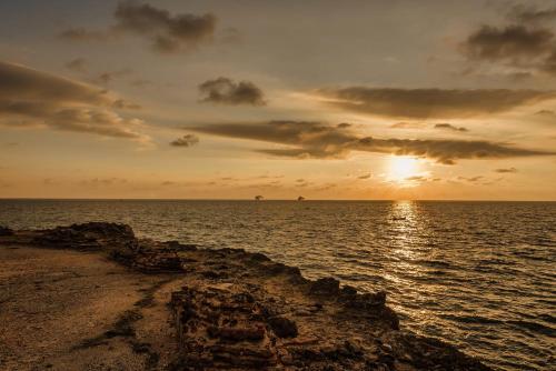 a sunset over the ocean with a rocky shore at Castillete Hotel & Beach Club in Tierra Bomba