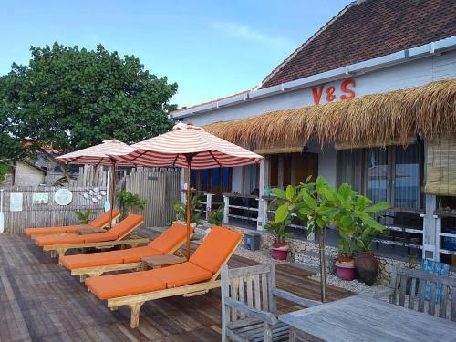 una fila di sedie arancioni e ombrelloni su un patio di VnS Beachfront Guesthouse a Nusa Penida