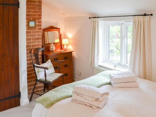 um quarto com uma cama, uma janela e uma cadeira em Lavenham Red Brick Cottage em Lavenham