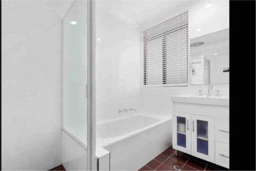 a white bathroom with a tub and a sink at Kiama beachside apartment in Kiama