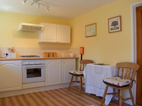cocina con armarios blancos, mesa y sillas en The Byre, en Lympsham
