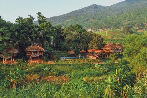 a group of houses in a field with mountains in the background at Pù Luông Ecolodge in Pu Luong