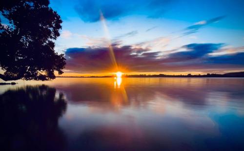 a sunset on a lake with the sun setting at Harbour View Motel and Waterfront Apartments in Tauranga