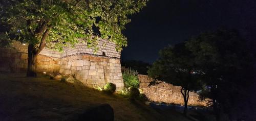 Una pared de piedra con un árbol delante de él por la noche en The Stair House en Suwon