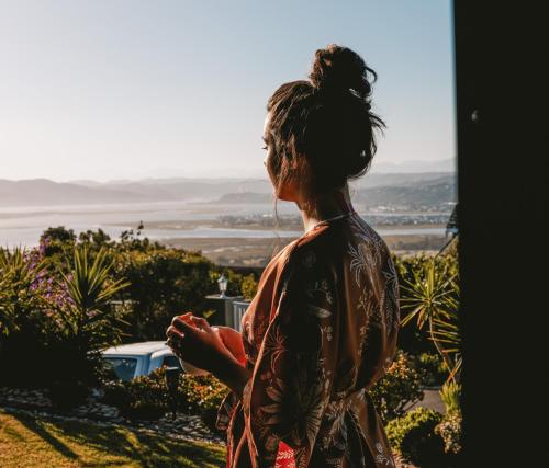 a woman looking out of a window at the ocean at Pezula Magic Escape - Guest House - No Loadshedding in Knysna