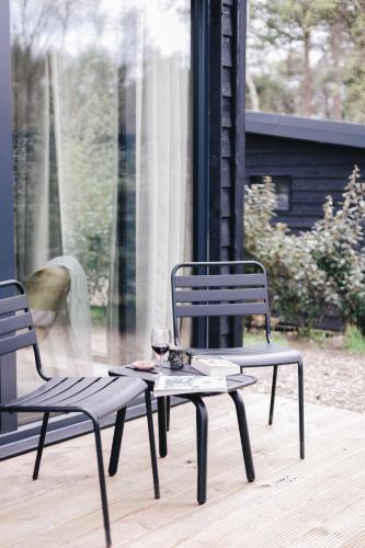 two chairs and a table with a glass of wine at Ultiem ontspannen in luxe en design ingericht tiny house in bosrijke omgeving in Nunspeet