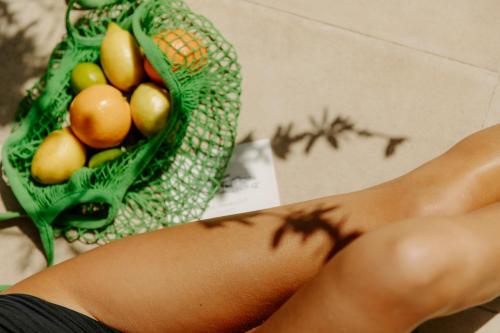 a woman sitting on the floor with a green bag of fruit at Oustau Camarguen Hôtel & Spa in Le Grau-du-Roi