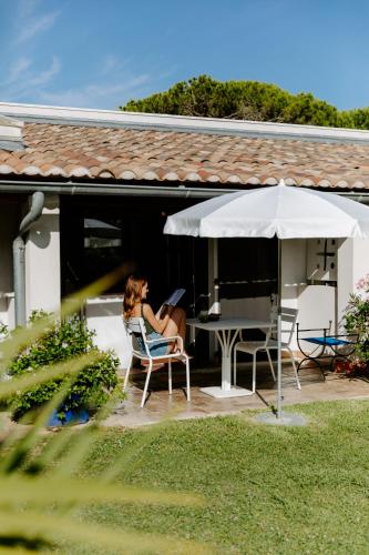 a woman sitting in a chair under an umbrella at Oustau Camarguen Hôtel & Spa in Le Grau-du-Roi