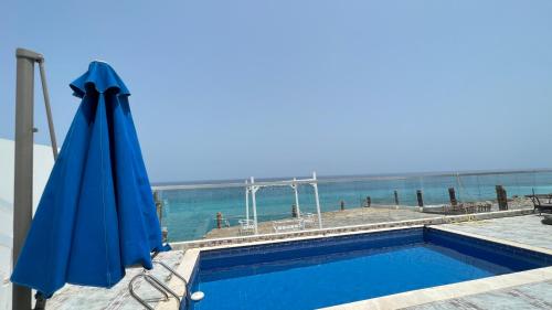 a blue swimming pool with an umbrella and the ocean at Wadi Shab Beach Villa in Sur