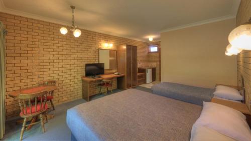 Un dormitorio con dos camas y un escritorio con televisión. en Barrass's John Bright Motor Inn, en Bright
