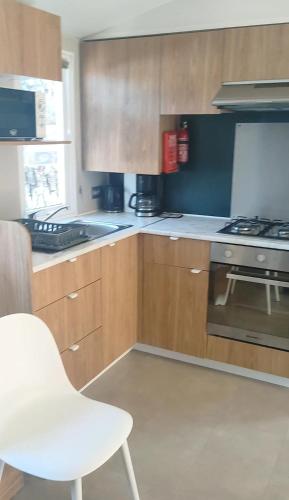 a kitchen with wooden cabinets and a white chair at Mobil home spacieux in Seignosse