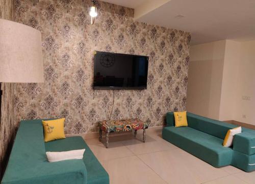 sala de estar con 2 sofás verdes y TV de pantalla plana en The Ganges View Luxury Penthouse by iTvara en Rishīkesh