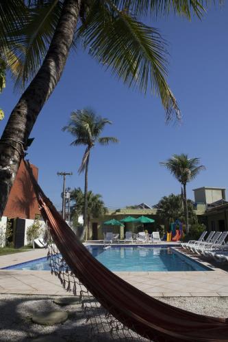 a hammock in front of a pool with palm trees at Hotel Vicino al Mare - Frente mar in Guarujá