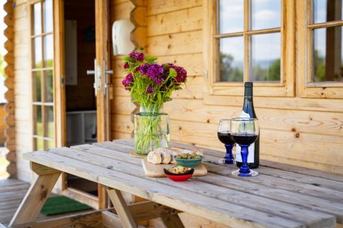 a wooden table with a vase of flowers and a glass of wine at Pastures Green Cabin (Oak Tree Lane) in Okehampton