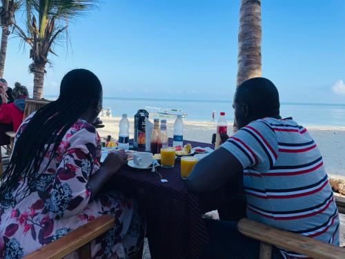 a man and woman sitting at a table at the beach at Aquarium Beach House in Nungwi