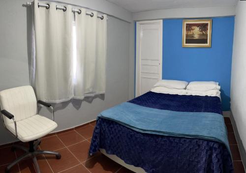 a bedroom with a bed and a white chair at Dith's House (kitnet 1) in Campos do Jordão
